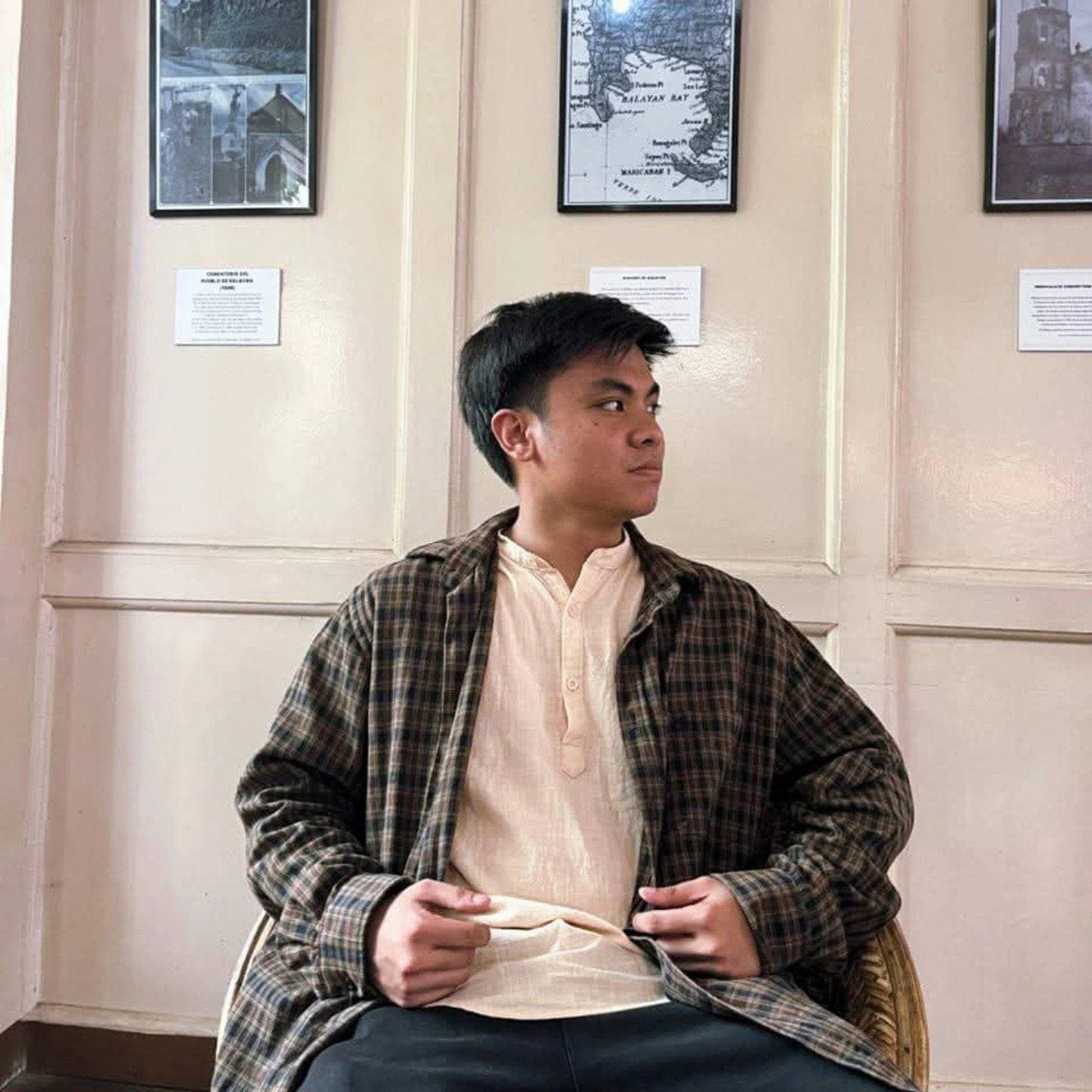 Linux Adona seated in a rattan chair in front of framed maps of Balayan Bay
